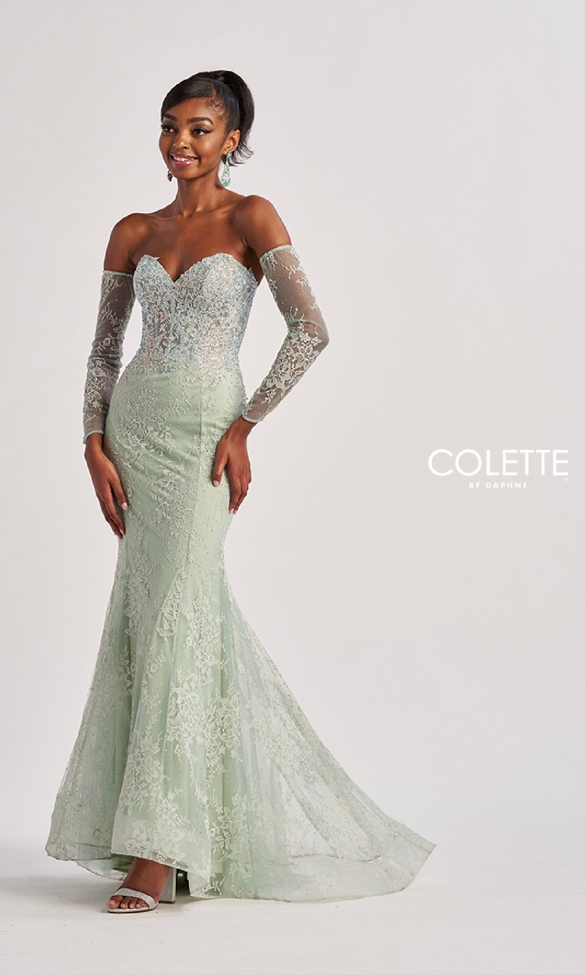 A woman models the Strapless Long Lace Prom Dress: Colette CL8415 in light green, smiling in front of a plain backdrop. This elegant gown perfectly fuses timeless sophistication with contemporary flair.